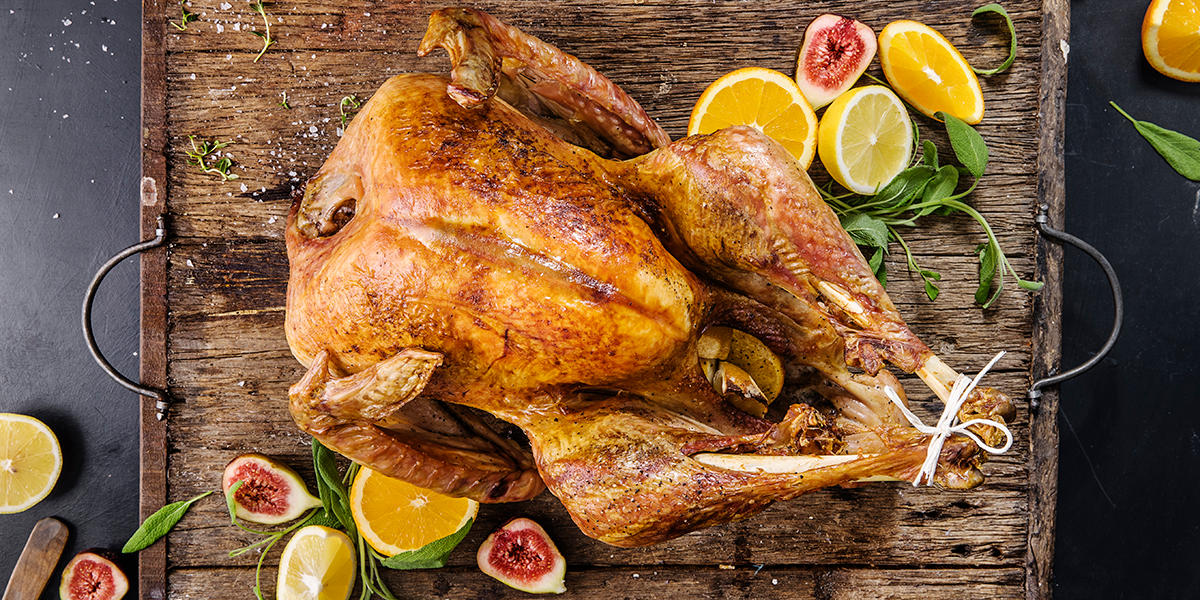 Saftig helstekt kalkun med gyllent skinn servert på rustikk trefjøl med ferske urter, sitronskiver, appelsinskiver og delte fiken.