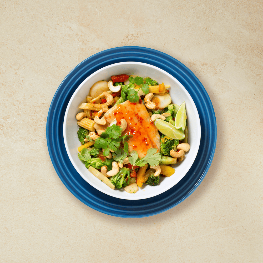 Sei med asiatisk vri, wokmiks, lime, cashewnøtter og chilisaus, i en hvit skål som står på en mørk blå tallerken