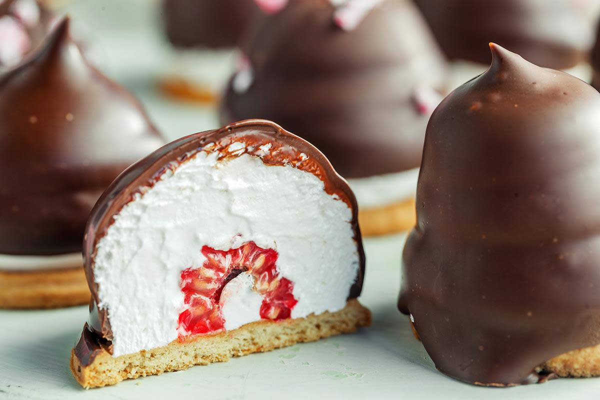 Hjemmelagede kokosboller med bringebær i midten, overtrukket med sjokolade. En kokosbolle er delt i to så man ser bringebæret i midten.