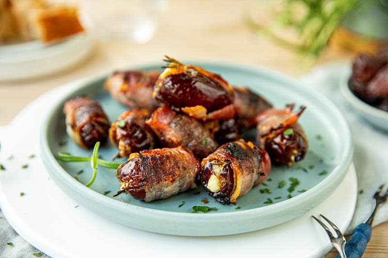 Fylte dadler med bacon fylt med kremost og rosmarin, servert på lyseblå tallerken på dekket bord.