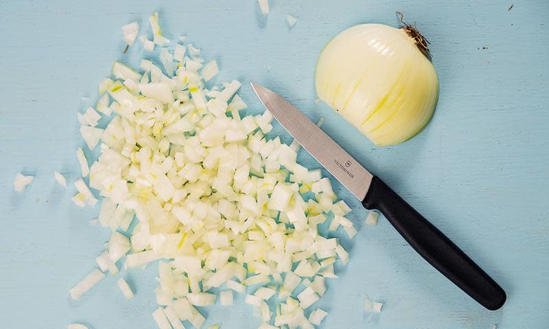 Haug med oppkuttet løk ved siden av en liten kniv, og en halv løk ved siden av. Blå bakgrunn.