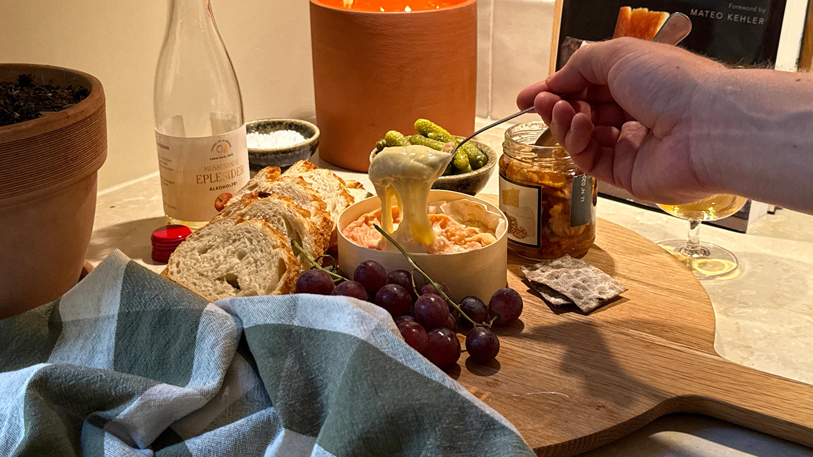 Ovnsbakt Epoisses de Bourgogne servert på rundt trefat med baguette, kjeks, røde druer, cornichons og valnøtter i honning fra Smak. Hånd holder en skje med smeltet ost.