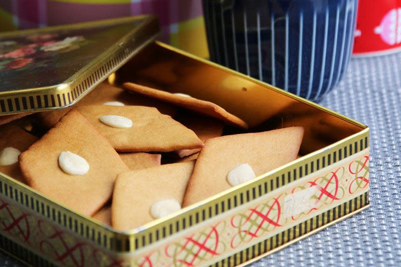 Gylne sirupsnipper med mandel i midten, servert i julekakeboks på kaffebord med duk.