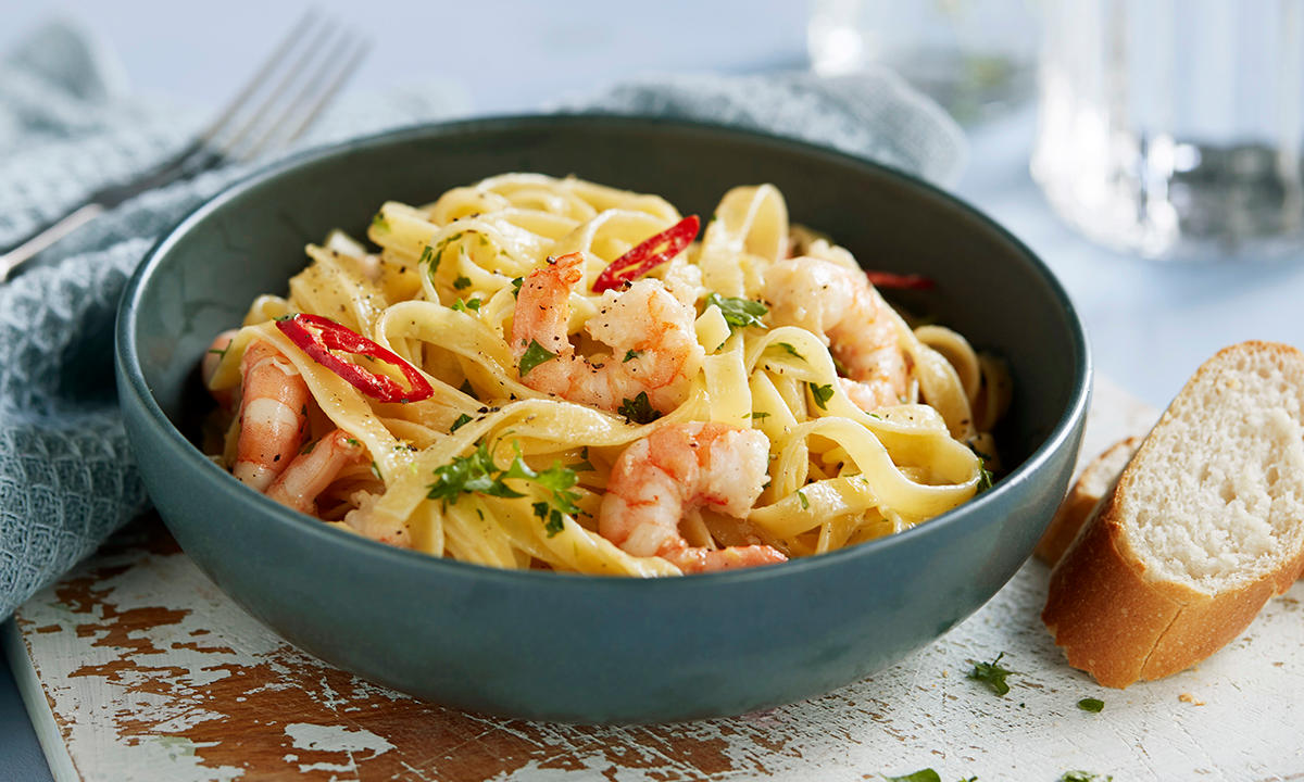 Pasta med scampi og chili servert i blå skål på rustikk lyst middagsbord, med to skiver baguette ved siden av.