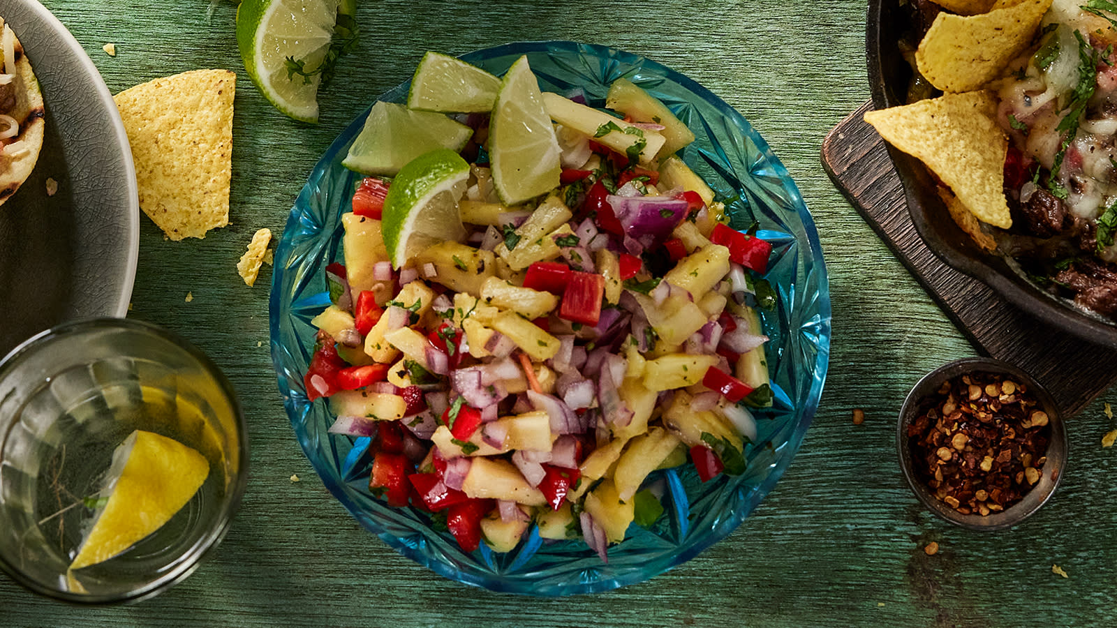 Mangosalsa med paprika, rødløk og tomat, servert i blå glassbolle med limebåter på siden.