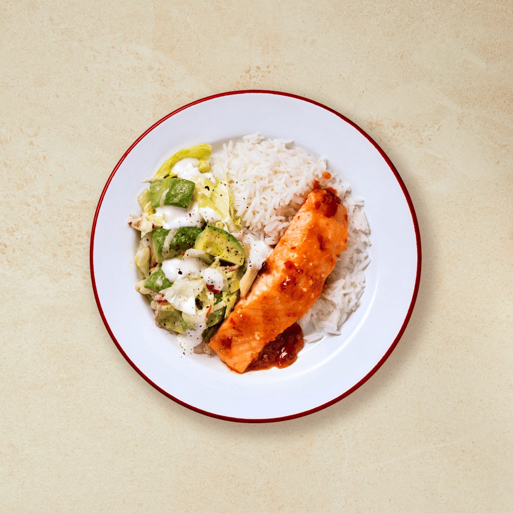 Laks, kremet salat og ris på en hvit tallerken med rød kant.