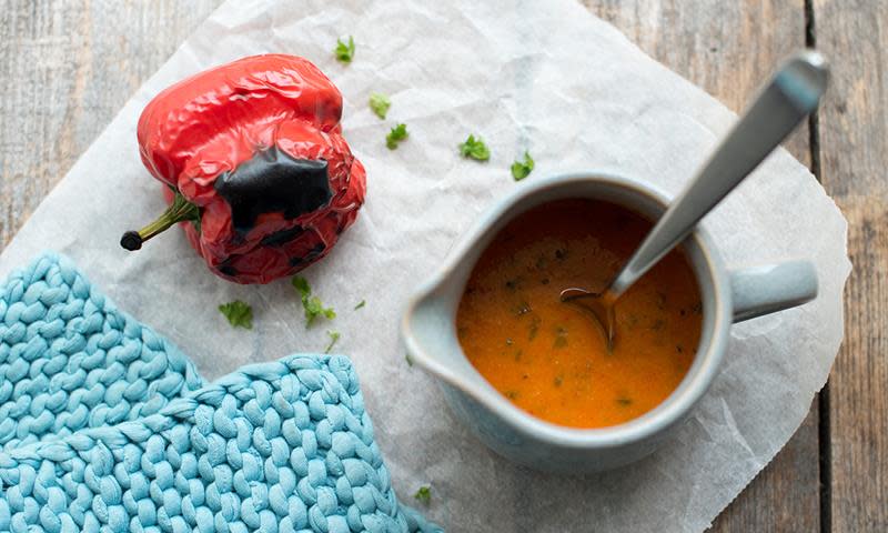 Grillet paprikasaus til hvit fisk, i hvitt sausenebb, på rustikk trebakgrunn. Grillet paprika og lyseblå grytekluter ved siden av.