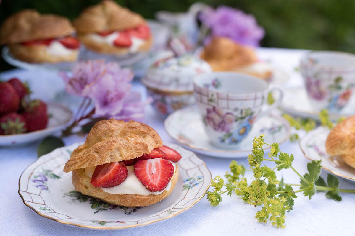 Hjemmelagede vannbakkels delt i to, fylt med luftig vaniljekrem og skiver av ferske jordbær. Servert på småblomstret teservise, på hyggelig dekket sommerbord i hagen.