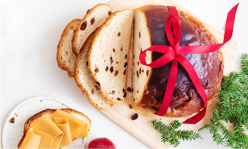 Saftig julebrød med rosiner, halvveis skåret opp og servert på lys trefjøl, med rødt bånd rundt.