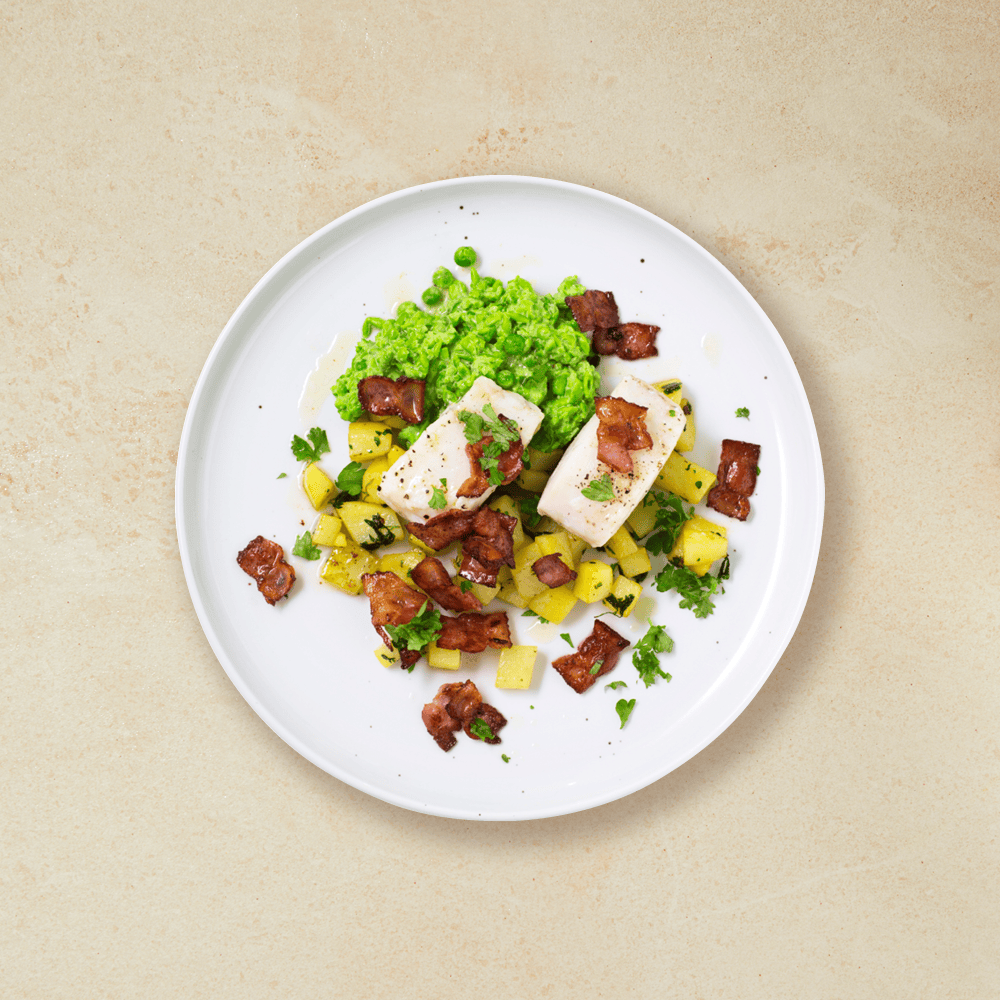 Ovnsbakt torsk med bacon og ertemos, servert på hvit tallerken med et dryss ferske urter over. Beige bakgrunn.