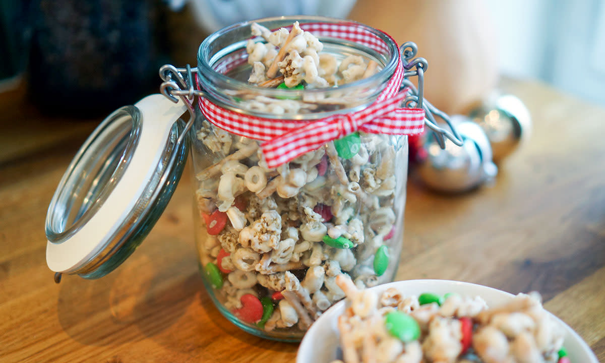 Reindeer Chow - hjemmelaget julegodis av frokostblanding, smeltet hvit sjokolade og non stop, pakket på syltetøyglass med rødt og hvitt bånd rundt.