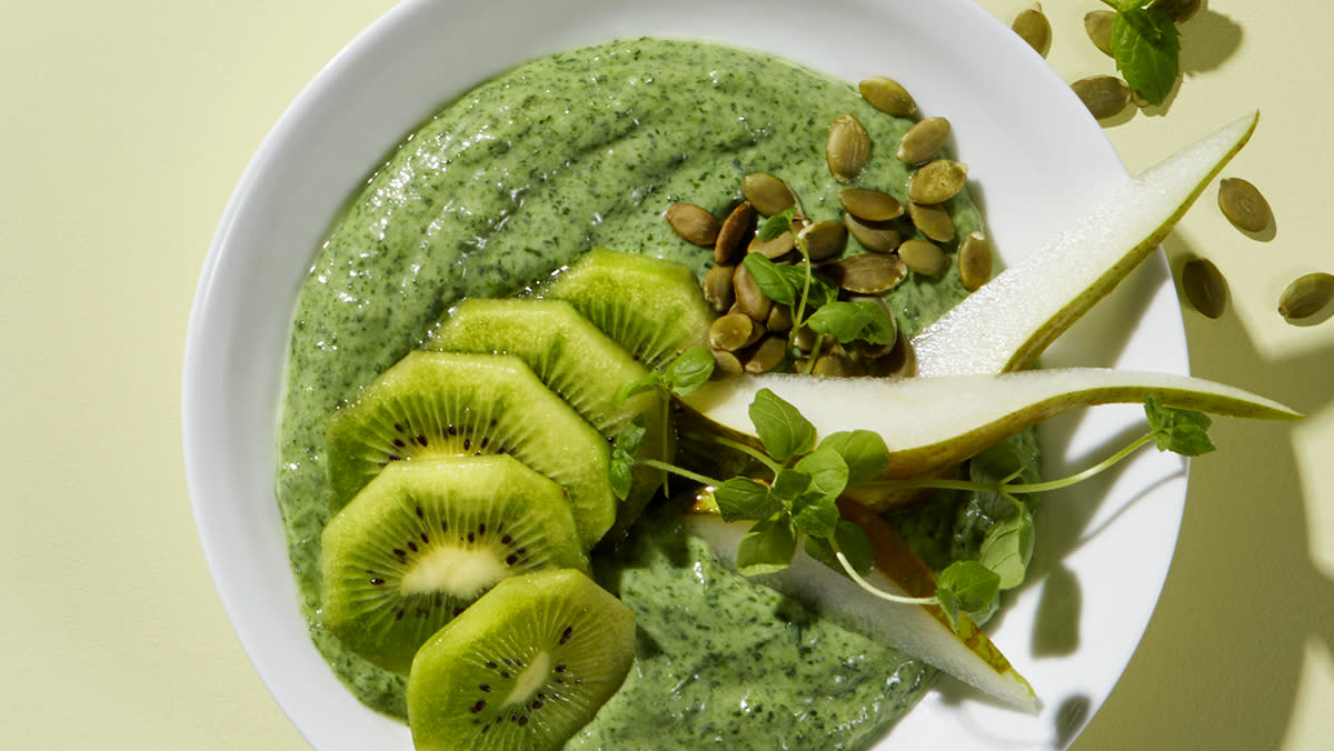 Sunn smoothiebowl toppet med kiwi, pære, gresskarkjerner og mynte.