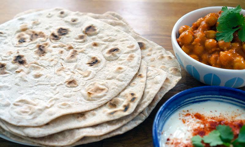 Chapati - Raskt Indisk hverdagsbrød, ligger i stabel på trebord. Skåler med raita og masala med kikerter ved siden av.