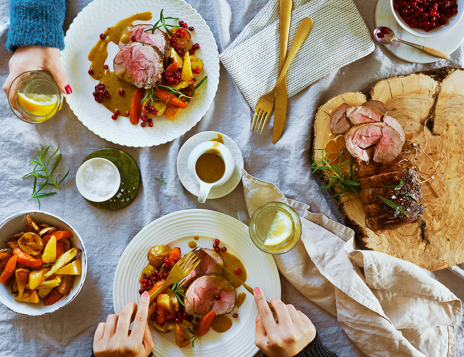 Lammestek med bakte rotgrønnsaker og sennepssjy servert på hvit tallerken. Hel lammestek med skiver skåret av på trefjøl ved siden av.