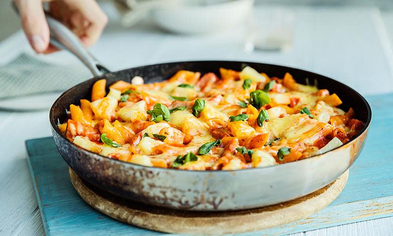 Pasta Hawaii med skinke og ananas, laget med pasta penne i stekepanne. Blå trebakgrunn.