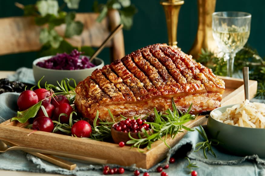 Langtidsstekt ribbe med sprø svor, hjemmelaget surkål og rødkål, servert på trefat på dekket julepyntet bord.