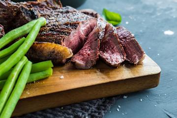 Entrecote hvor deler av kjøttet er skjært i tynne skiver og aspargesbønner ved siden av på et trefat