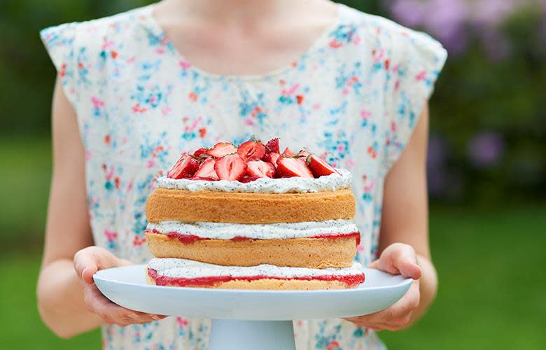 Naken sommerkake med ostekrem og ferske bær servert på hvitt stettfat som holdes frem av kvinne med blomstrete kjole.