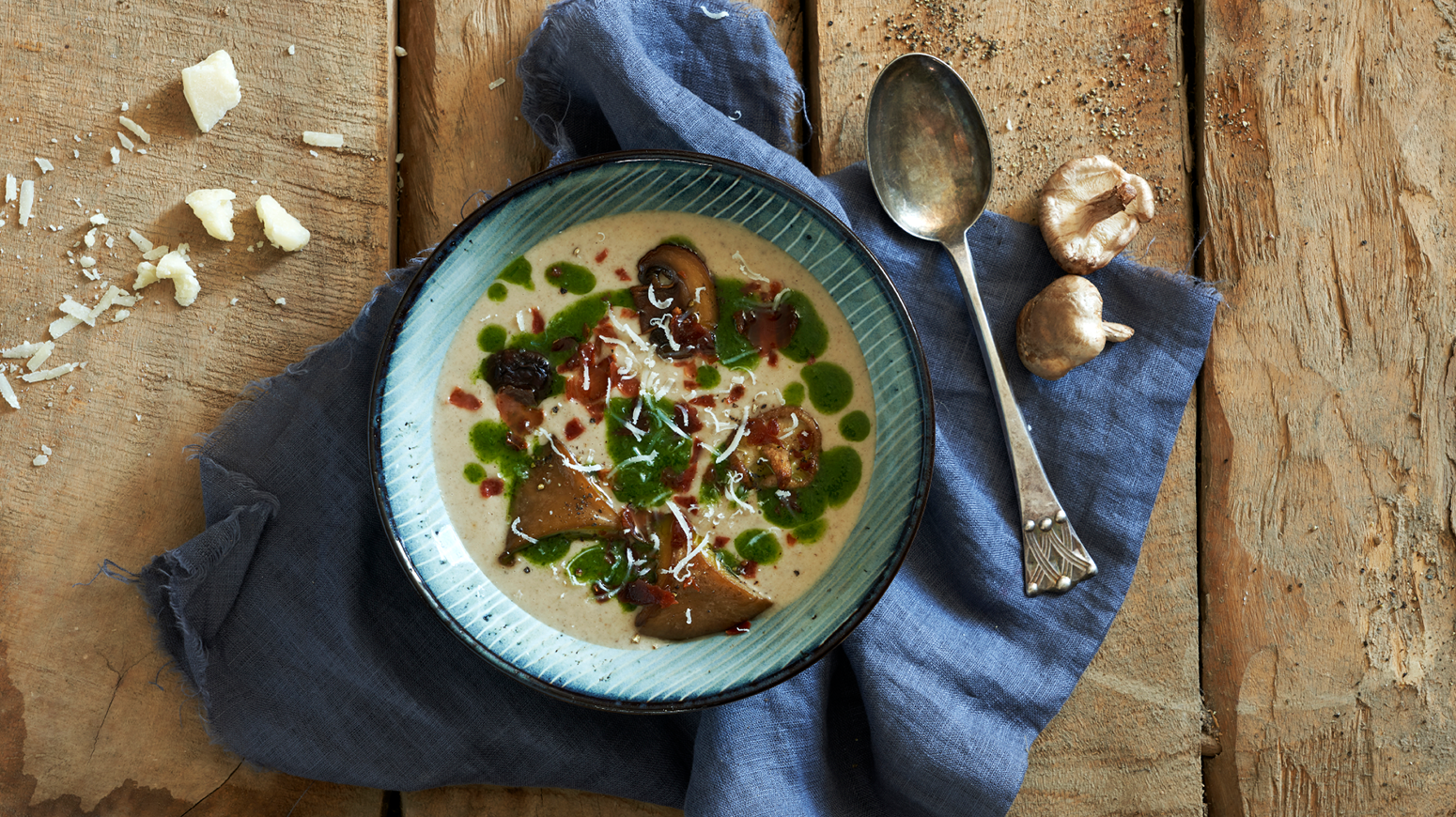 Skogsoppsuppe med gresskarolje i en skål på trebord med en blå stoffserviett.