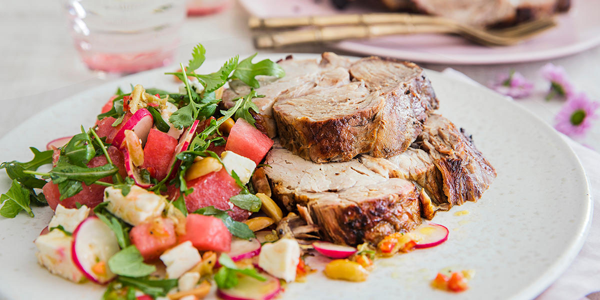 Hvitløksmarinert svinenakke, skåret i skiver og servert på hvit tallerken med vannmelonsalat med reddik, fetaost, ruccola og peanøtter.