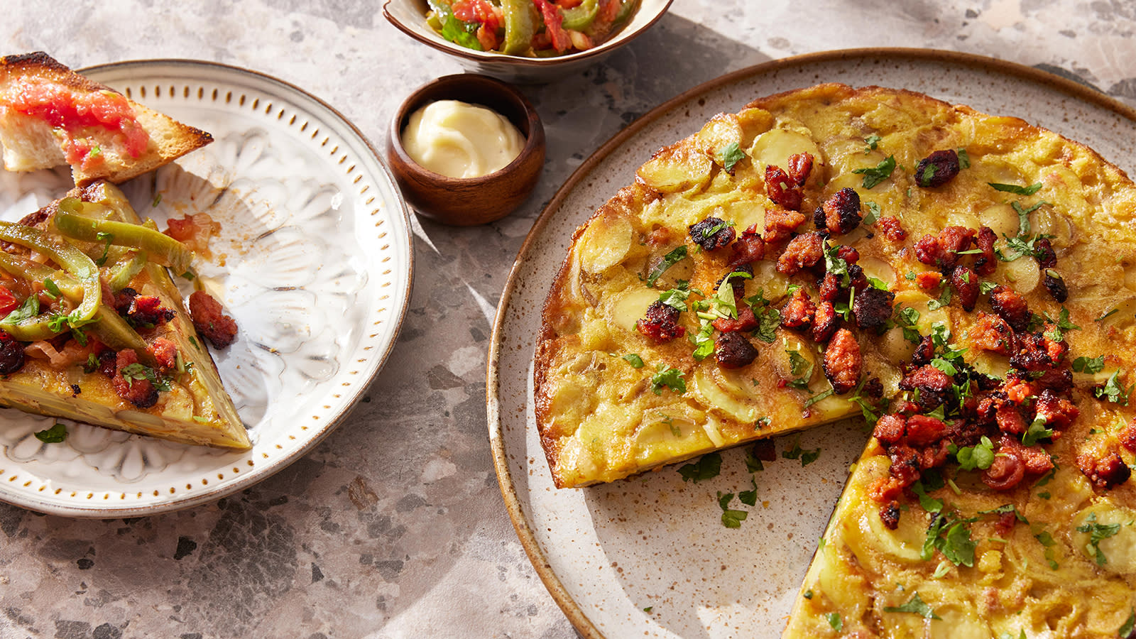 Spansk omelett med chorizo servert på lyst keramikkfat med en bit omelett på liten asjett ved siden av.