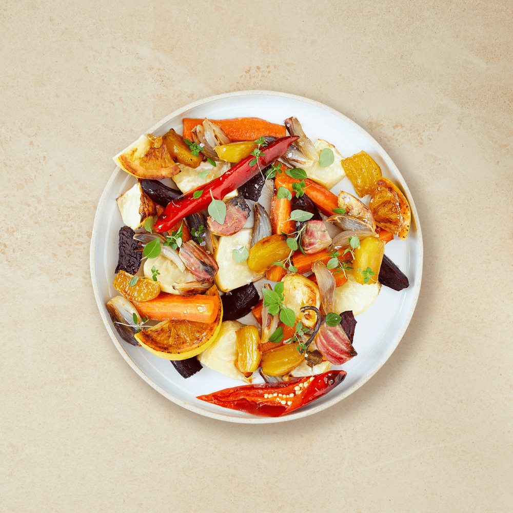 Ovnsbakte rotgrønnsaker med sitron og chili servert på hvit tallerken, på hvit bakgrunn.