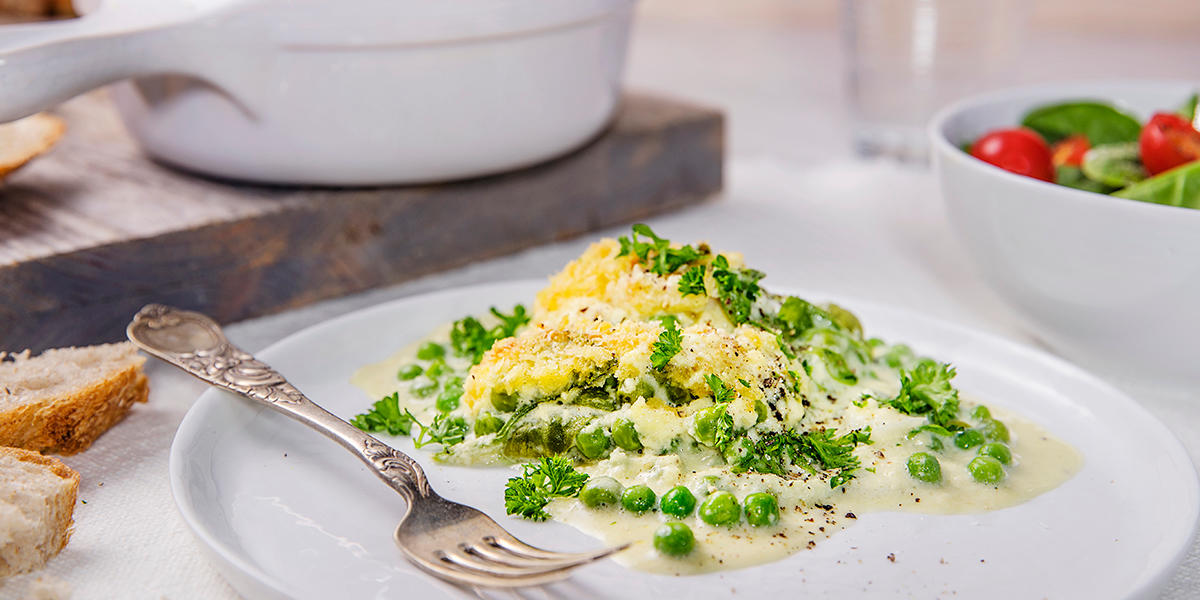 Grønn fiskegrateng med lettsaltet torsk, erter og spinat, servert på hvit tallerken.