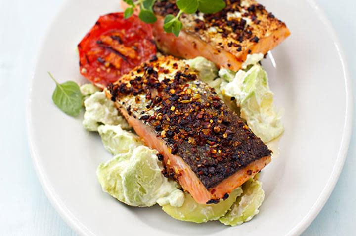 Stekt laks med kremet avokadosalat og stekt tomat, ligger på hvit middagstallerken med skinnsiden opp. Ferske urter på toppen.