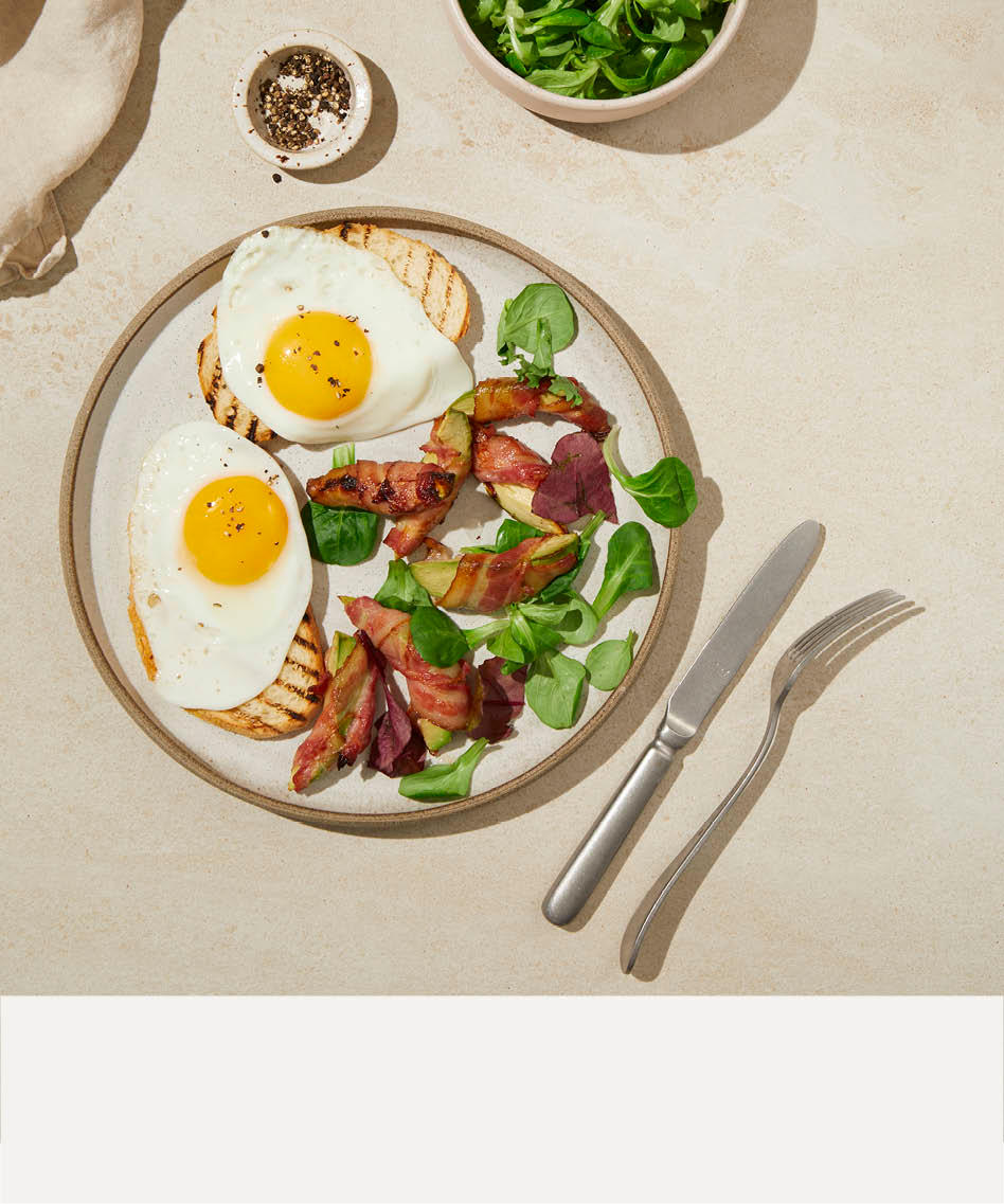 To toast med speilegg, bacon og basilikum på en tallerken med en beige stripe nederst