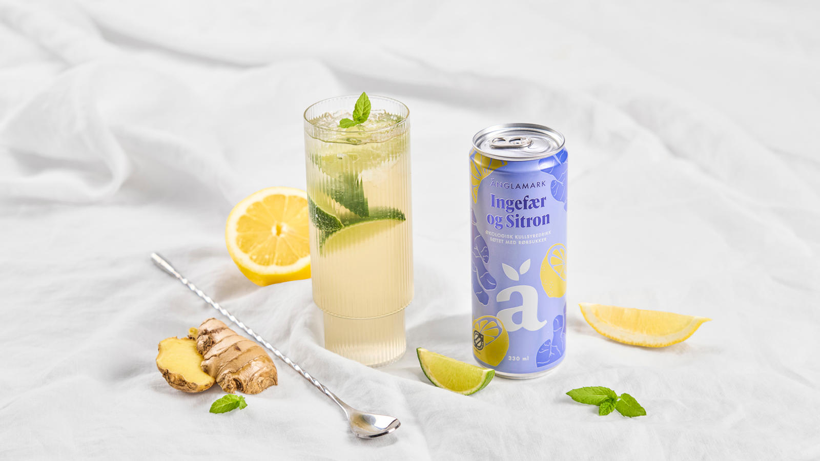 Minty Mule mocktail i highball glass med Änglamark Ingefær og Sitron drikke ved siden av. Frisk lime, mynte og ingefær rundt.