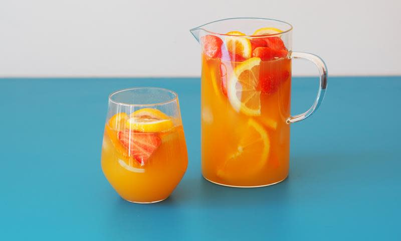 Alkoholfri punsj med appelsinskiver og jordbærskiver, servert i mugge, med glass med punsj ved siden av. Blå bakgrunn.