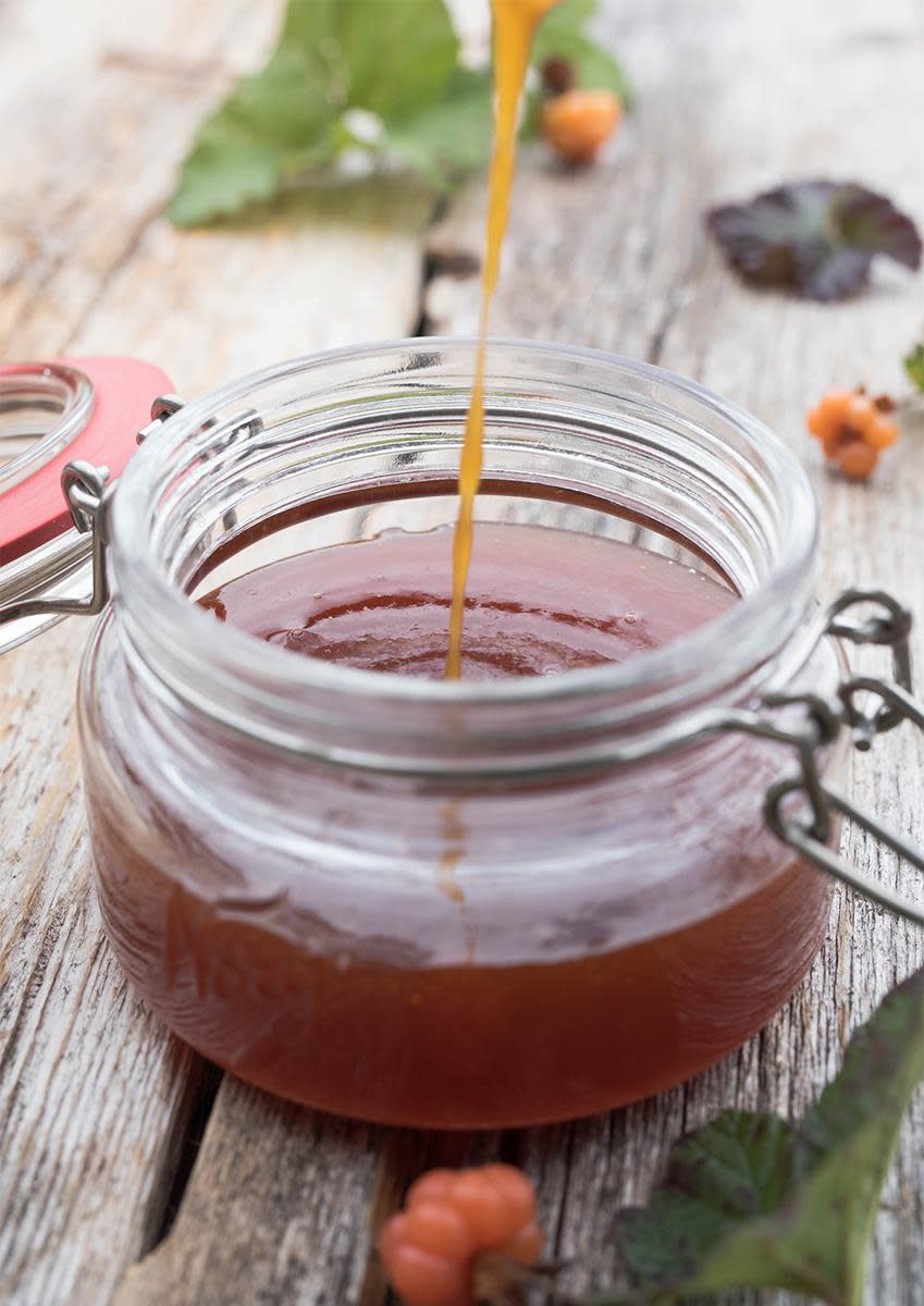 Hjemmelaget multesirup helles i Norgesglass, på rustikk trebord. Ferske multer og grønne blader omkring.