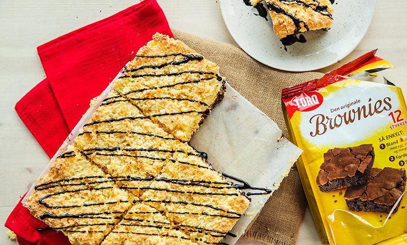 Julebrownies i langpanne med kokosmakron på toppen, og sjokoladesaus ringlet over. Pose med Toro brownies-miks på siden. Rød linserviett under kaken.