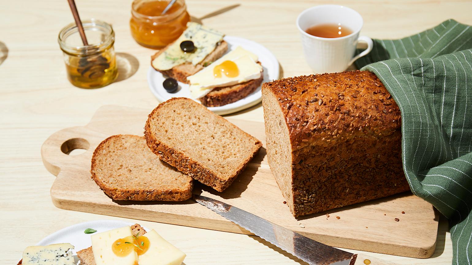 Grovbrød skåret i skiver og servert på lys trefjøl. Små asjetter med brød og ost rundt.