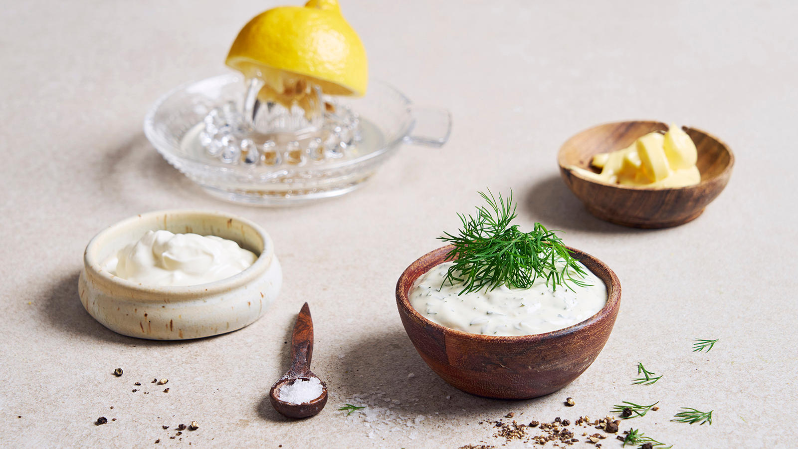 Dilldressing til skalldyr servert i liten mørk treskål med frisk dill på toppen. Små skåler majones og lettrømme ved siden av, og sitronpresse med sitron bak.