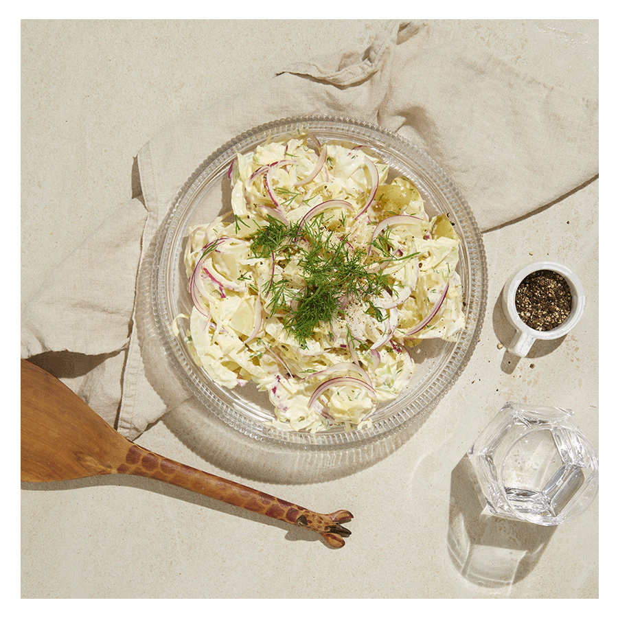 Kremet potetsalat med purre, fennikel og rødløk, servert i gjennomsiktig glassbolle med dill på toppen.