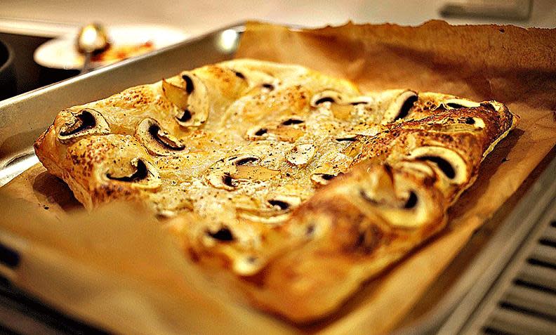 Butterdeigspizza med sopp og kremost, på bakepapirkledd stekebrett.