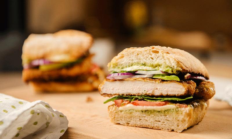 Italiensk kyllingsandwich med pesto og mozzarella, delt i to og servert på trefjøl.