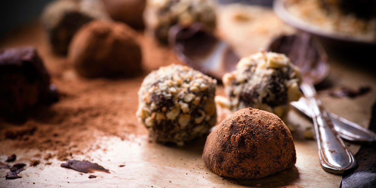 Hjemmelaget konfekt i form av kuler rullet i hakkede nøtter og kakaopulver. Kulene ligger på bakepapir med kakaopulver og sjokolade.