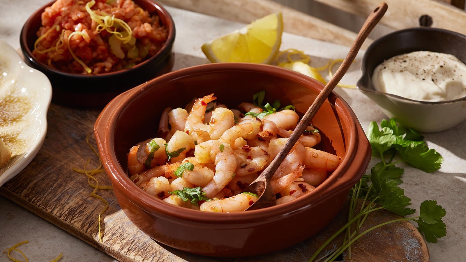 Scampi i hvitløksolje med spansk ris servert i ildfaste former på rustikk trefjøl. Skål med aioli ved siden av.