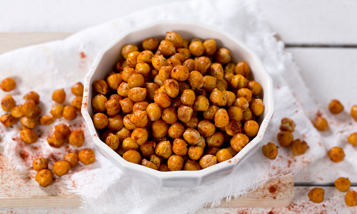 Ovnsristede kikerter med chili servert i hvit skål på lys trefjøl, på hvitt trebord.