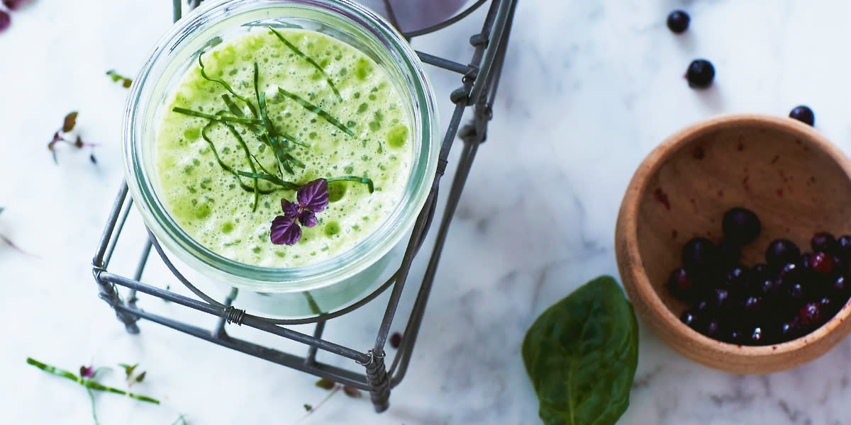 Supergrønn smoothie i glass på marmorbord, toppet med finstrimlet spinat og lilla urteblader.