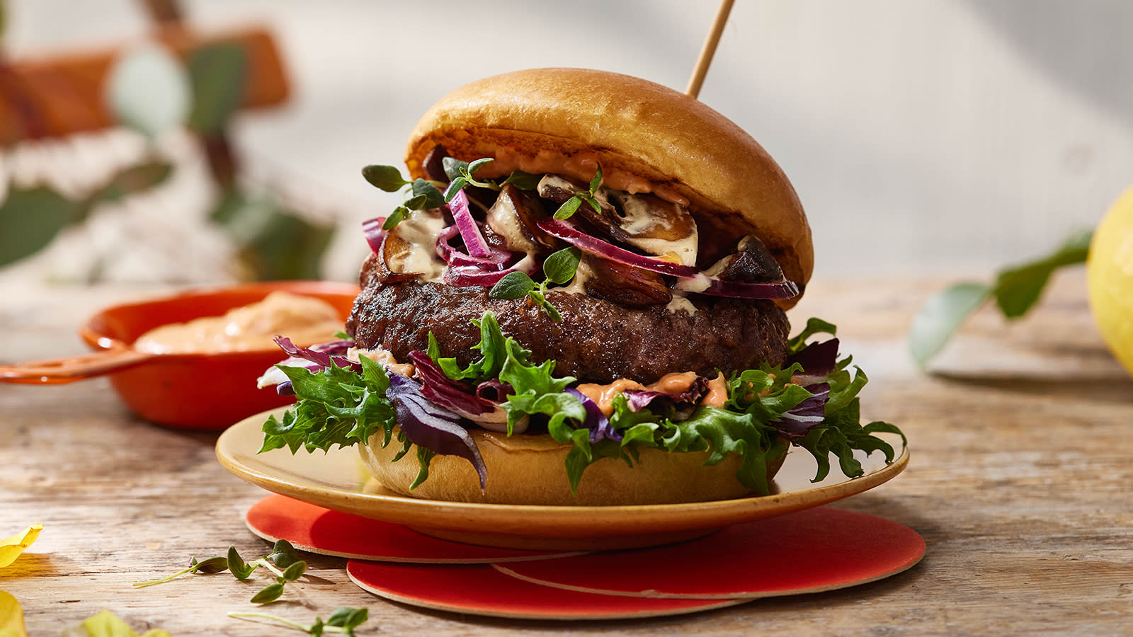 Big Beefy Burger med kremet sopp og karamellisert løk servert med salat, rødløk og dressing på lys tallerken på rustikk trebord.