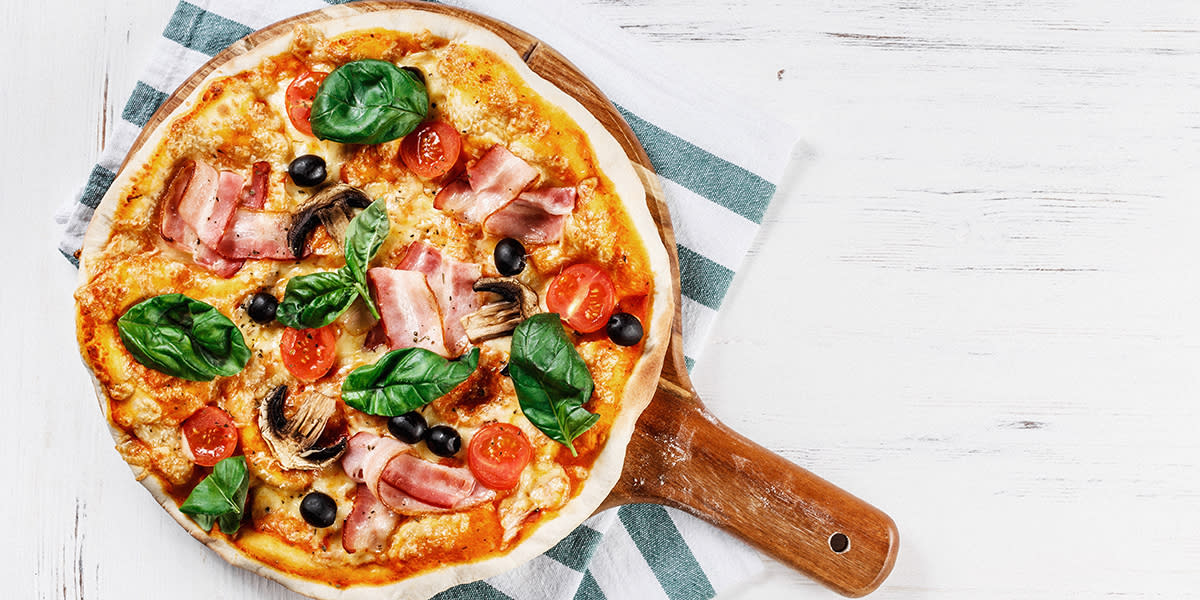 Hjemmelaget italiensk pizza med bacon, tomater, oliven, sopp og basilikum sett ovenfra.