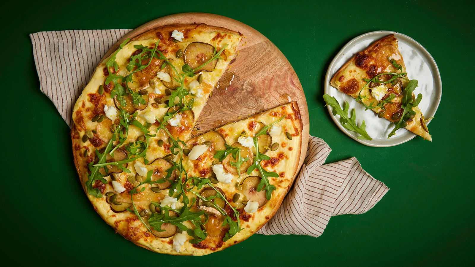 Hvit vegetarpizza med chèvre og pære servert på rund trefjøl med ruccola på toppen.