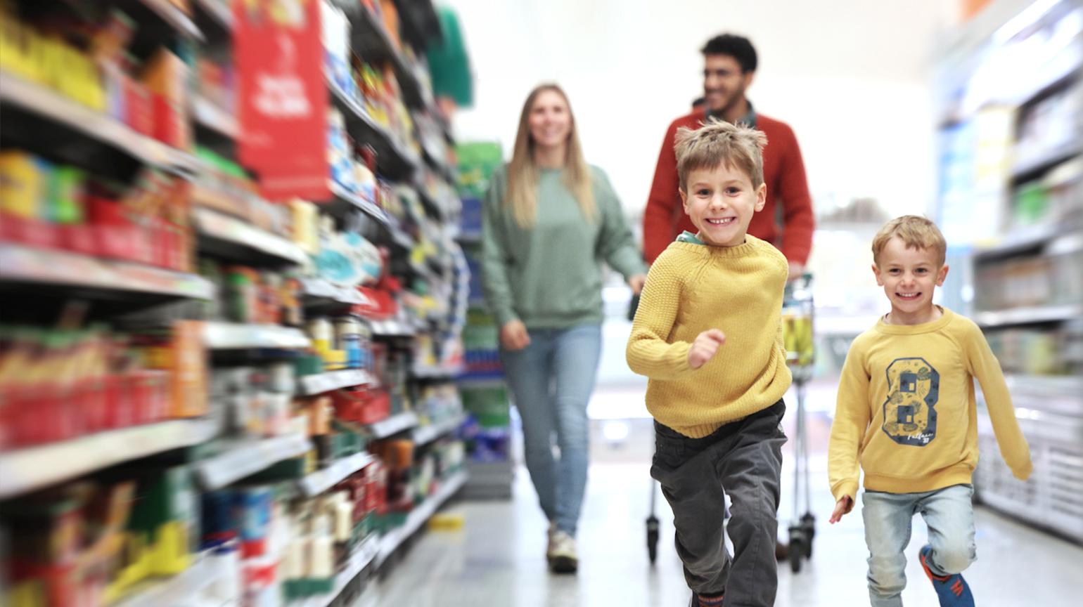 To gutter som løper i en dagligvarebutikk med foreldrene bak