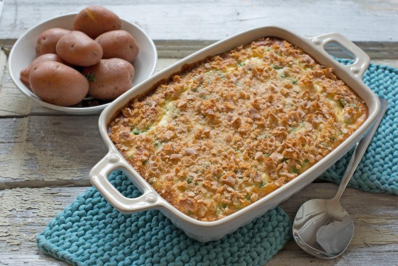 Gylden hjemmelaget fiskegrateng, servert i lys ildfast form, på lyseblå grytelapper. Kokte poteter på siden.