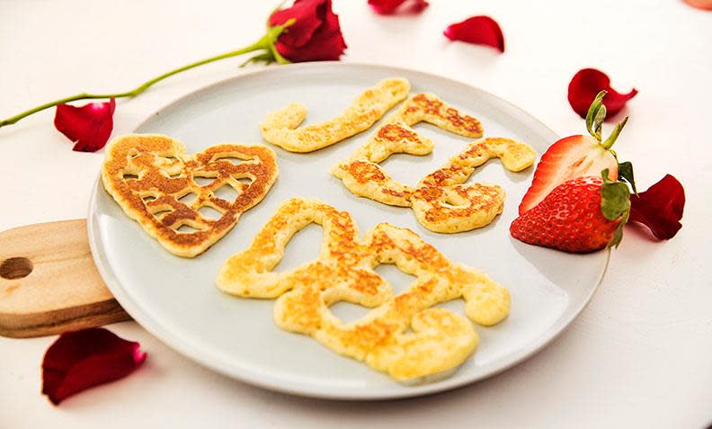 Jeg elsker deg - pannekaker, pannekakerøre formet til ordene "Jeg elsker deg" og stekt i panne. Servert på hvit tallerken, med ferske jordbær og en rød rose.