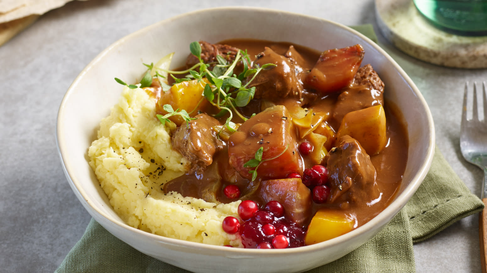 Kjøtt i mørke med rotmiks og syrlig potetmos servert i hvit skål med tyttebærsyltetøy og frisk timian.