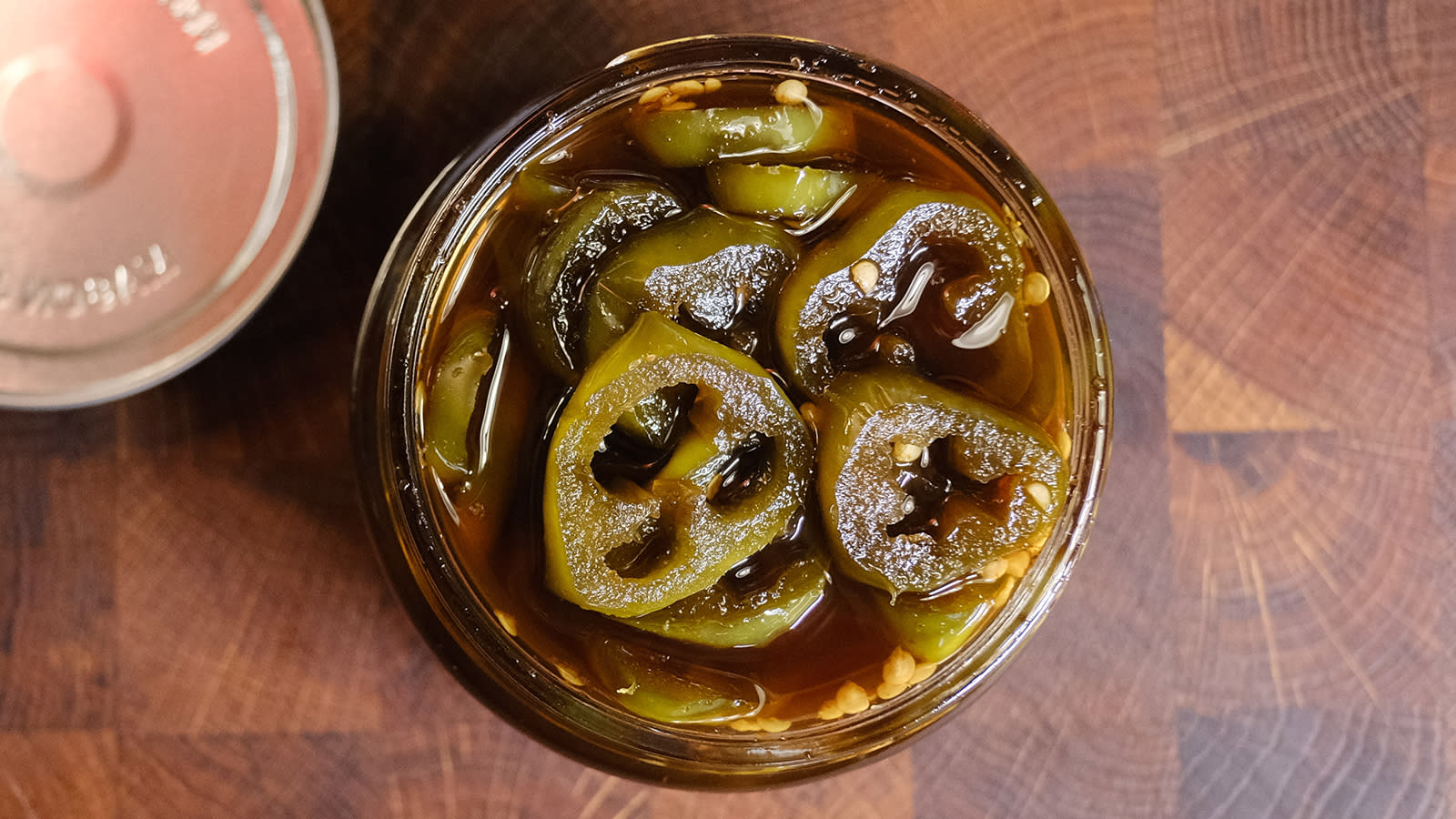 Cowboy Candy - karamelliserte jalapeños, servert i syltetøyglass med lokket ved siden av.